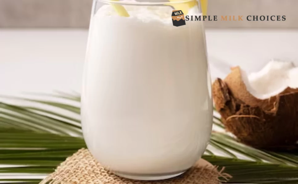 Glass of creamy coconut milk placed beside a halved coconut on a wooden surface
