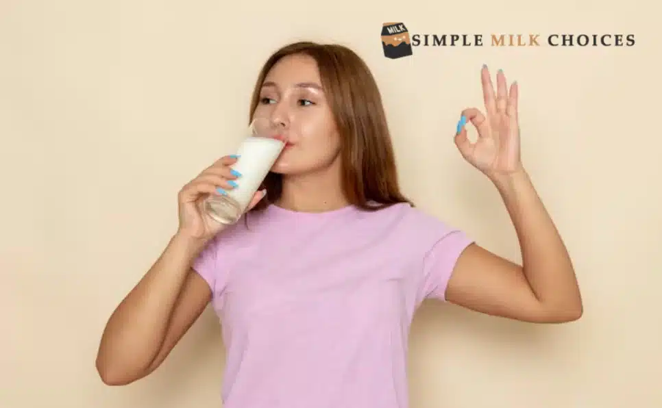 Smiling girl enjoying a glass of almond milk, showing an 'OK' hand gesture, endorsing the benefits of drinking almond milk for a healthy lifestyle.